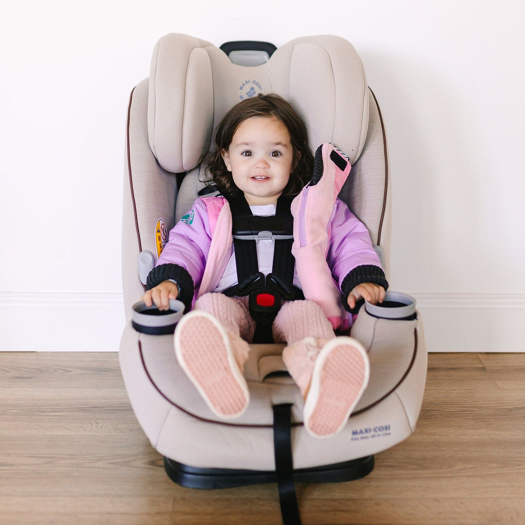 Powerpuff/Pink/Purple
A toddler girl is wearing a pink and purple carseat coat and sitting in a tan car seat.  The coat is open showing the buckled harness.  The girl is smiling at the camera.