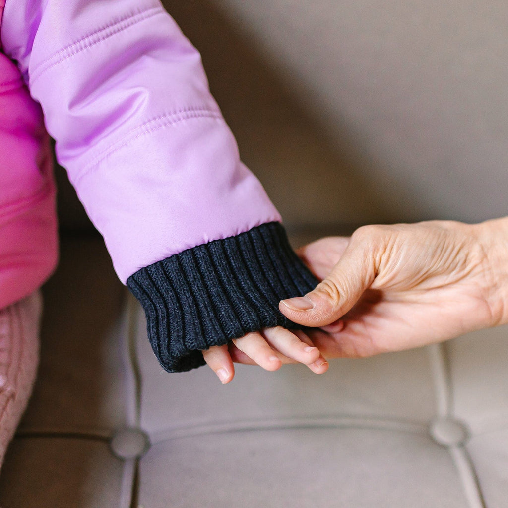 Powerpuff/Pink/Purple
A child and adult are holding hands.  The child is wearing a pink and purple carseat coat.  The photo is zoomed in on the purple sleeve and charcoal extendable cuff of the coat.  