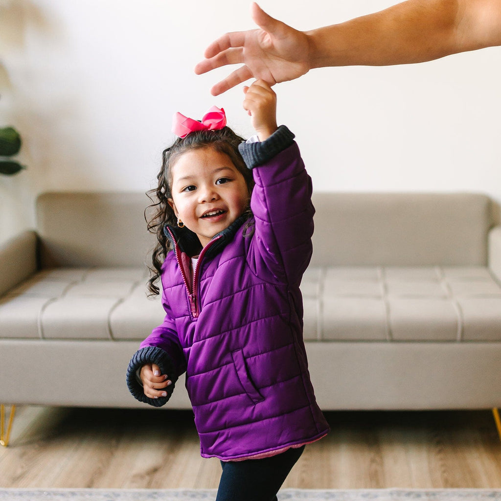 The Jam/Maroon
Little girl with curly brown hair and a pink bow is wearing a purple car seat coat.  She is holding an adults finger while smiling at the camera.